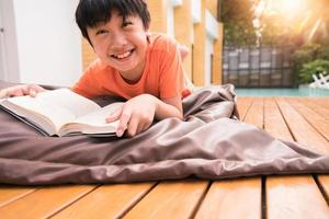 um menino sorrindo com um livro na mesa de madeira. aprendendo em casa foto