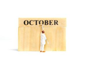 pessoas em miniatura, trabalhador pintando outubro em um bloco de madeira em fundo branco. foto