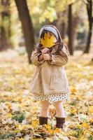 menina feliz segurando uma folha de bordo amarela no parque outono foto