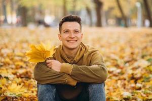 menino com um buquê de folhas sorrindo e sonhando no parque outono foto