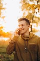 cara feliz sorrindo e falando ao telefone no parque de outono foto