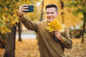 cara sorrindo e segurando um buquê de folhas e tirando uma selfie no parque foto