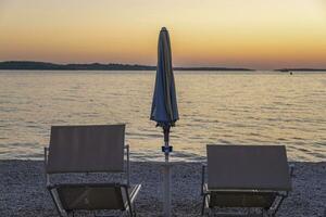 cenário do a pôr do sol em a de praia do a croata costeiro Cidade do fazana com Sol espreguiçadeira e sombrinha foto