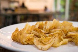 pilha de pão indiano frito e crocante de roti em um prato branco com leite doce foto