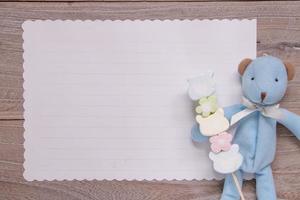 mesa de madeira, papel carta branca, boneca de urso azul segurando algodão doce foto