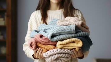 uma mulher segurando grande pilha do guardada tricotado caloroso colorida camisolas, fácil chique estilo, diferente tricô padrões. generativo ai foto