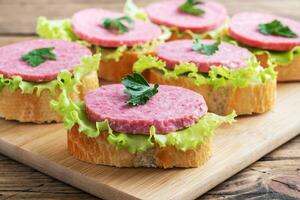 sanduíches com folhas de alface e linguiça de salame fatiada em uma placa de madeira. foto