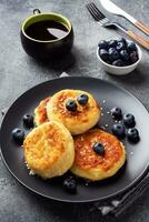 bolinhos de queijo cottage com mirtilos. cheesecakes de queijo coalho, panquecas em um fundo escuro de concreto. copie o espaço. foto