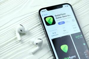 Carcóvia, Ucrânia - marcha 5, 2021 guitarra ícone e inscrição a partir de aplicativo loja em Iphone 12 pró exibição tela com airpods pró em branco mesa foto