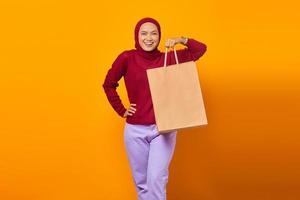 alegre mulher asiática segurando sacolas de compras sobre fundo amarelo foto