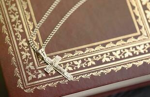 colar de prata com cruz crucifixo no livro da bíblia sagrada cristão na mesa de madeira preta. pedindo bênçãos de deus com o poder da santidade, que traz sorte foto