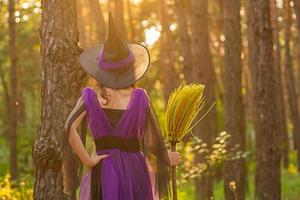 jovem com uma fantasia de halloween na floresta com uma vassoura foto