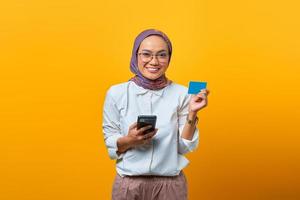 alegre mulher asiática segurando um smartphone e mostrando um cartão em branco