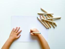 pequeno criança desenha com colori lápis em papel em branco mesa. em branco folha. foto