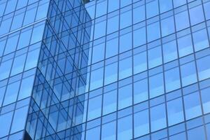 vidro construção com transparente fachada do a construção e azul céu. estrutural vidro parede refletindo azul céu. abstrato moderno arquitetura fragmento. contemporâneo arquitetônico fundo. foto