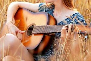 lindo jovem mulher sentado dentro trigo campo e jogando acústico guitarra. foto