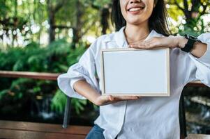 mulher sorridente segurando quadro branco no jardim foto