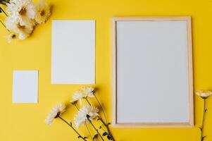 quadro branco, cartão em branco e flor são colocados em fundo amarelo foto