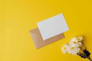 um cartão em branco com envelope e flor é colocado em fundo amarelo foto