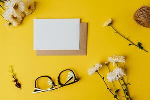 cartão em branco com envelope, óculos e flor é colocado em amarelo foto