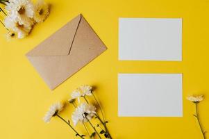 cartão em branco com envelope e flor é colocado em fundo amarelo