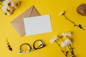 cartão em branco com envelope, óculos e flor é colocado em amarelo foto