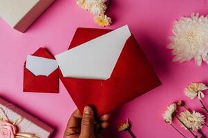 envelope vermelho, caixa de presente rosa com cartão em branco e flor foto