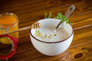 leite aveia mingau com querida para café da manhã dentro uma tigela de madeira mesa. foto