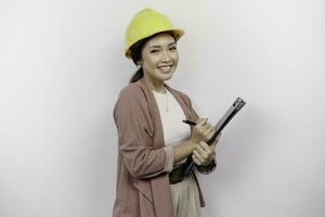 sorridente jovem ásia mulher empregado vestindo segurança capacete enquanto segurando uma prancheta, isolado de branco fundo foto