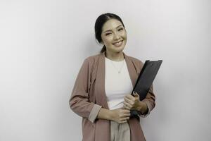 sorridente jovem ásia mulher empregado vestindo casaco enquanto segurando uma prancheta, isolado de branco fundo foto