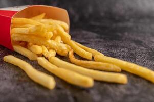 batatas fritas derramadas de um saco no chão de cimento preto. foto