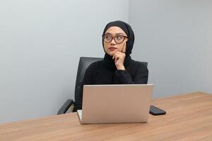 retrato do atraente ásia hijab mulher trabalhando em dela computador portátil. muçulmano menina sentindo-me Exausta e cansado. empregado e freelance trabalhador conceito. foto