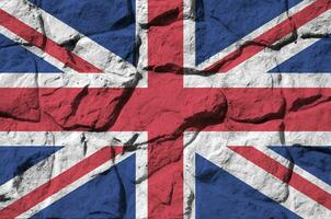 ótimo Grã-Bretanha bandeira retratado dentro pintura cores em velho pedra parede fechar-se. texturizado bandeira em Rocha parede fundo foto