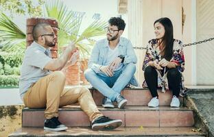 três jovem amigos falando sentado em a escadaria. três Adolescência amigos falando sentado em a escadaria, três jovem pessoas sentado em a rua conversando. conceito do amigos falando foto