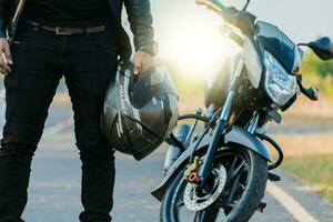 irreconhecível motociclista segurando capacete Próximo para moto perto a estrada. motociclista segurando segurança capacete Próximo para dele moto perto a estrada. motocicleta segurança capacete conceito foto