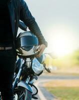 motocicleta segurança capacete conceito. irreconhecível motociclista segurando capacete Próximo para moto perto a estrada. motociclista segurando segurança capacete Próximo para dele moto perto a estrada foto