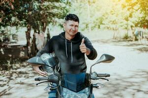 motociclista em dele moto segurando segurança capacete com polegar acima. conceito do sorridente motocicleta ciclista segurando segurança capacete, motociclista homem dando polegar acima enquanto segurando segurança capacete foto