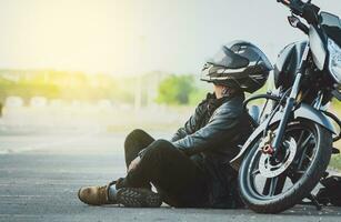 motociclista sentado Próximo para dele motocicleta em a estrada. masculino motociclista sentado e inclinado em dele motocicleta em a asfalto foto