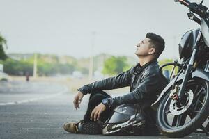 masculino motociclista sentado e inclinado em dele motocicleta em a asfalto. motociclista sentado Próximo para dele motocicleta em a estrada foto