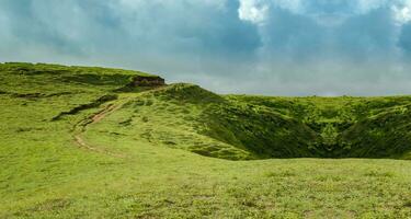 uma Colina cercado de de outros verde colinas, uma caminho para uma verde Colina com azul céu com cópia de espaço foto