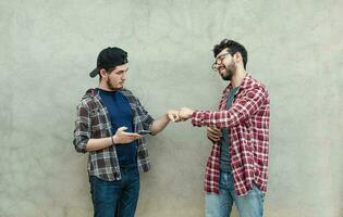 dois Adolescência amigos cumprimento cada de outros de punho batendo ao ar livre. dois sorridente jovem rapazes batendo punhos perto uma muro. conceito do dois sorridente amigos batendo punhos amigáveis foto