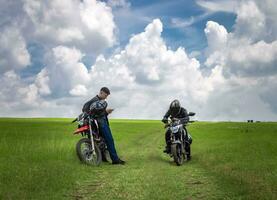 dois homens com seus motocicletas estacionado conversando dentro a campo, dois jovem motociclistas dentro a campo, dois homens em motocicletas em uma lindo país estrada, jovem motociclistas estacionado em uma estrada foto