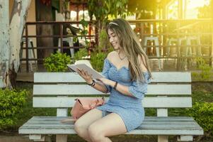 uma fofa menina sentado em uma Banco lendo uma livro, bonita jovem latim menina lendo uma livro em uma Banco foto
