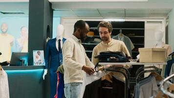 africano americano homem Perguntando assistente para Socorro com camisas, olhando para Comprar formal vestem em cabides. varejo loja empregado falando para cliente sobre compras para elegante roupas. tripé tomada. foto