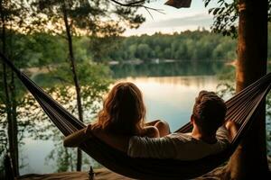 jovem casal em repouso dentro maca em a lago costa às pôr do sol, pessoa Visão casal em repouso às acampamento mulher deitado dentro maca com lindo Visão do floresta lago, ai gerado foto