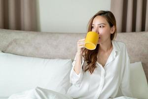 retrato de mulher bonita acordar e segurando uma xícara de café ou caneca na cama foto