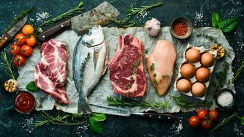 vários proteína fontes conceito - costela olho, salmão bife, carne de porco, ovo. topo visualizar. em uma Preto pedra fundo. foto