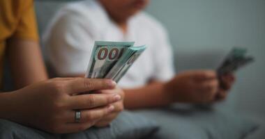 retrato fechar acima do jovem mulheres e adolescente menina contando dinheiro dinheiro em sofá dentro a vivo quarto às casa, feliz contando dólares nota de banco. foto