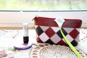 Cosmético bolsa, pó, batom com a artificial calla flor em uma guardanapo de a janela, horizontal foto