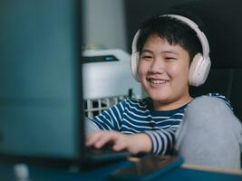 estilo de vida ásia pequeno Rapazes sorrir usar Área de Trabalho pcs computador para jogar profissional vídeo jogos com fones de ouvido dentro a casa, bate-papo com amigos, e entretenimento foto
